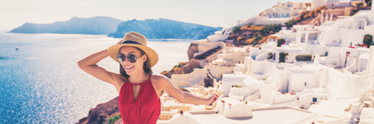 Woman in red dress and hat in front of a Greek island with white buildings